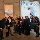 Visitantes disfrutando de la exposición NumEros en la calle, en un entorno urbano con cartel grande y ambiente nocturno. Grupo de personas posando frente a un cartel de la exposición NumEros en la calle.